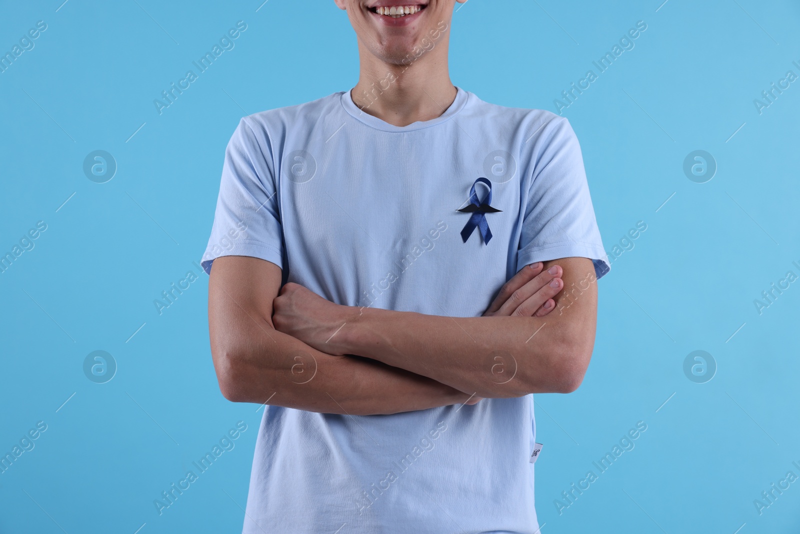 Photo of Prostate cancer awareness. Man with blue ribbon and fake mustache on color background, closeup