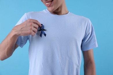 Prostate cancer awareness. Man with blue ribbon and fake mustache on color background, closeup