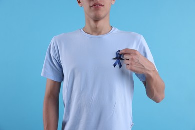 Prostate cancer awareness. Man with blue ribbon and fake mustache on color background, closeup