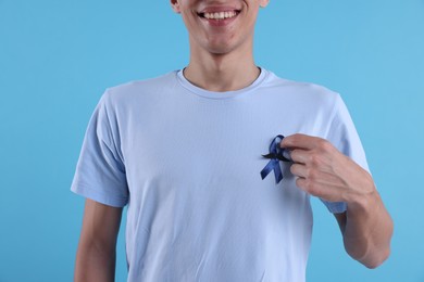 Photo of Prostate cancer awareness. Man with blue ribbon and fake mustache on color background, closeup