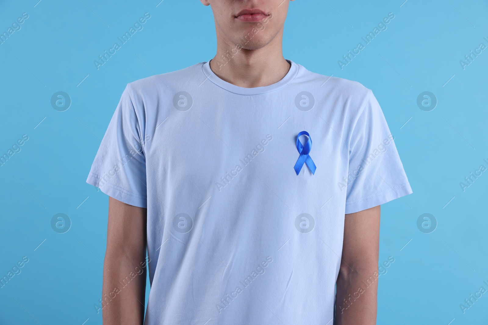 Photo of Prostate cancer awareness. Man with light blue ribbon as symbol of support on color background, closeup