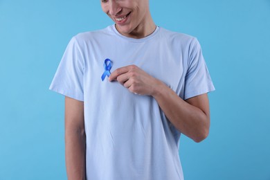 Photo of Prostate cancer awareness. Man with light blue ribbon as symbol of support on color background, closeup