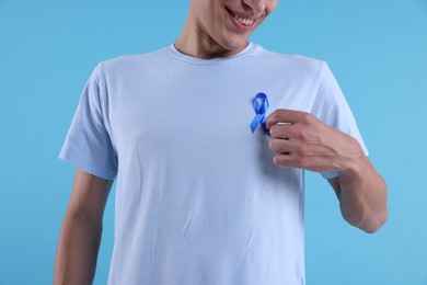 Photo of Prostate cancer awareness. Man with light blue ribbon as symbol of support on color background, closeup
