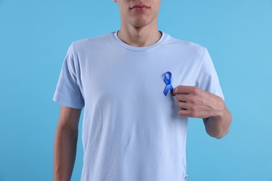 Photo of Prostate cancer awareness. Man with light blue ribbon as symbol of support on color background, closeup