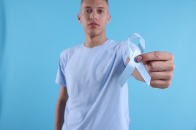 Photo of Prostate cancer awareness. Man holding light blue ribbon as symbol of support on color background, selective focus