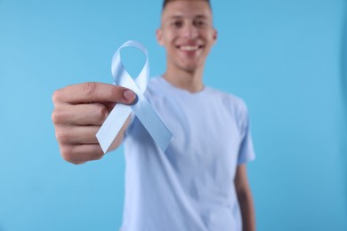 Photo of Prostate cancer awareness. Man holding light blue ribbon as symbol of support on color background, selective focus