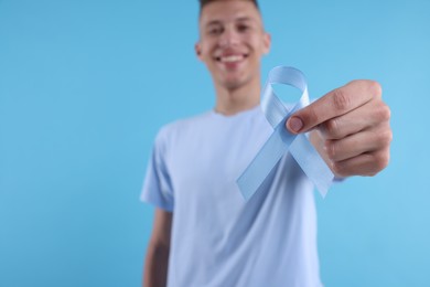 Photo of Prostate cancer awareness. Man holding light blue ribbon as symbol of support on color background, selective focus