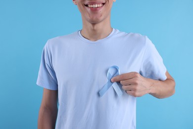 Photo of Prostate cancer awareness. Man holding light blue ribbon as symbol of support on color background, closeup