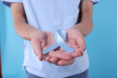 Photo of Prostate cancer awareness. Man holding light blue ribbon as symbol of support on color background, closeup