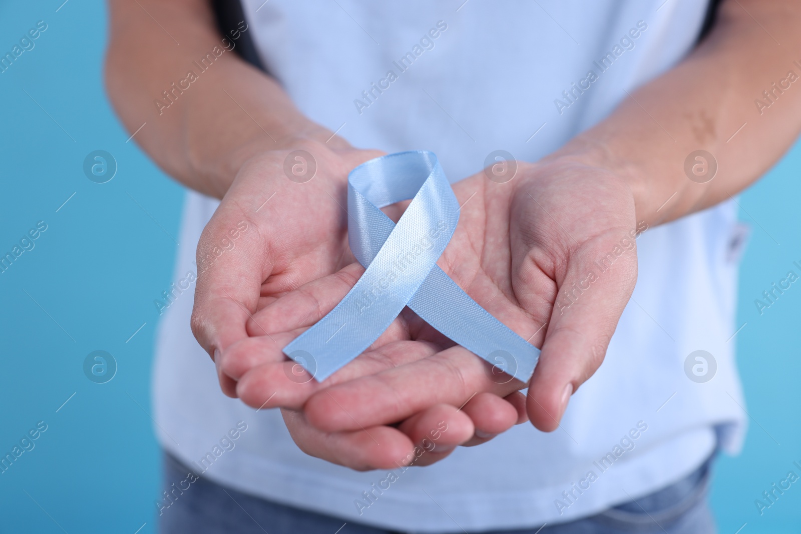 Photo of Prostate cancer awareness. Man holding light blue ribbon as symbol of support on color background, closeup