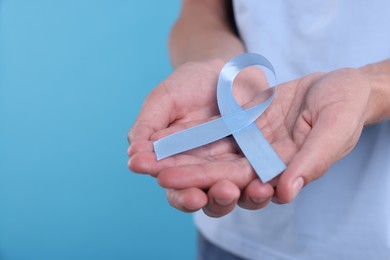 Photo of Prostate cancer awareness. Man holding light blue ribbon as symbol of support on color background, closeup. Space for text