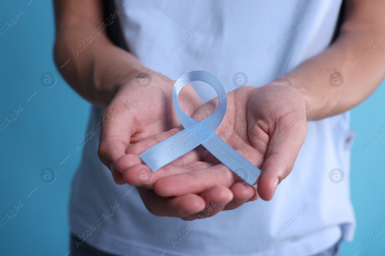 Photo of Prostate cancer awareness. Man holding light blue ribbon as symbol of support on color background, closeup