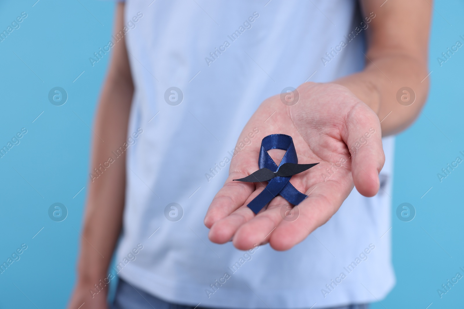 Photo of Prostate cancer awareness. Man holding blue ribbon with fake mustache on color background, closeup