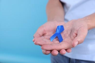 Photo of Prostate cancer awareness. Man holding blue ribbon as symbol of support on color background, closeup. Space for text