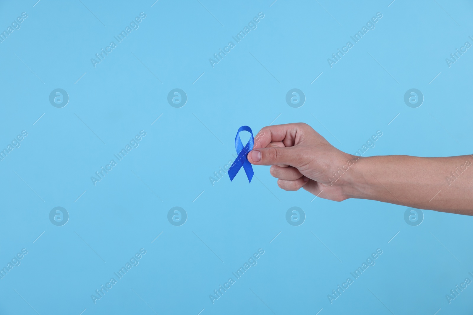 Photo of Prostate cancer awareness. Man holding blue ribbon as symbol of support on color background, closeup. Space for text