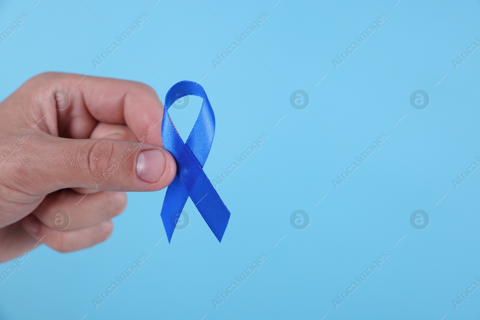 Photo of Prostate cancer awareness. Man holding blue ribbon as symbol of support on color background, closeup. Space for text