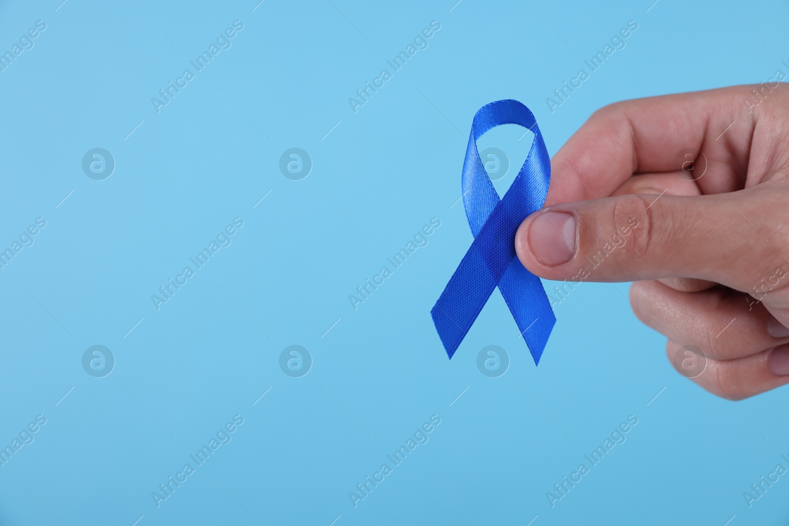 Photo of Prostate cancer awareness. Man holding blue ribbon as symbol of support on color background, closeup. Space for text