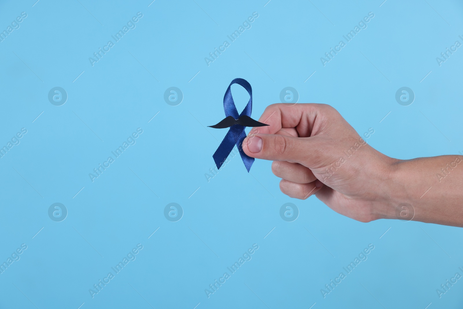 Photo of Prostate cancer awareness. Man holding blue ribbon with fake mustache on color background, closeup. Space for text