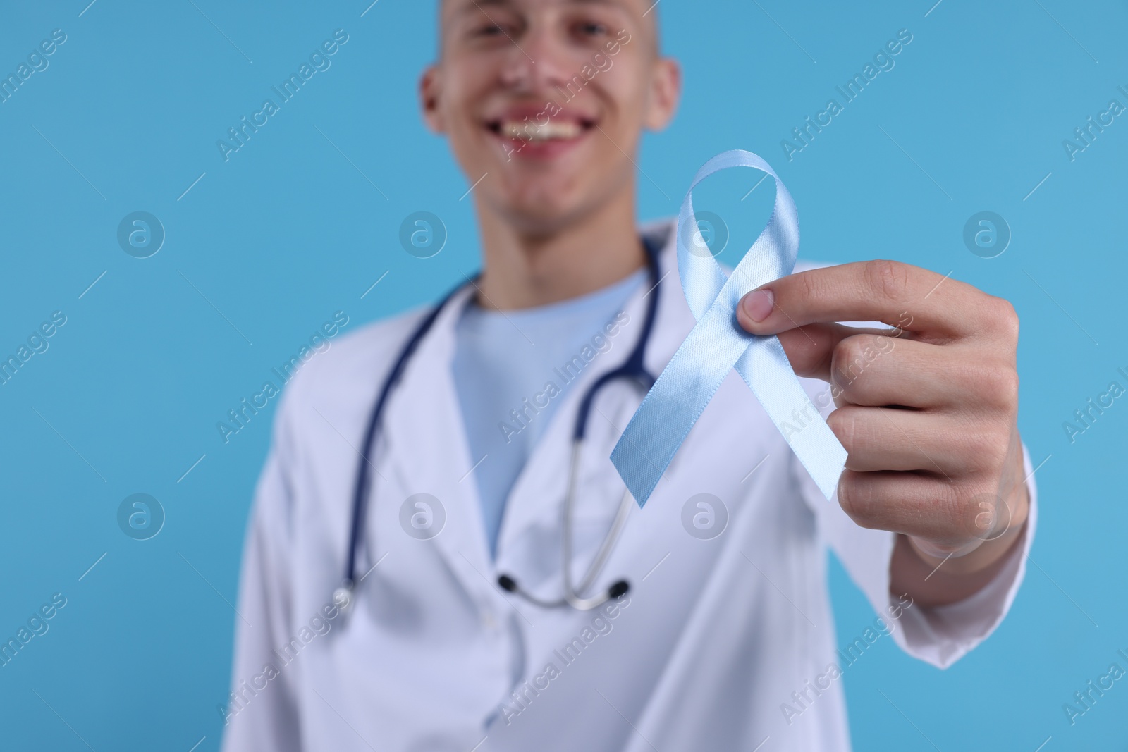 Photo of Prostate cancer awareness. Doctor holding light blue ribbon as symbol of support on color background, selective focus