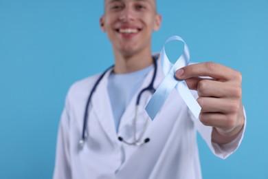 Prostate cancer awareness. Doctor holding light blue ribbon as symbol of support on color background, selective focus