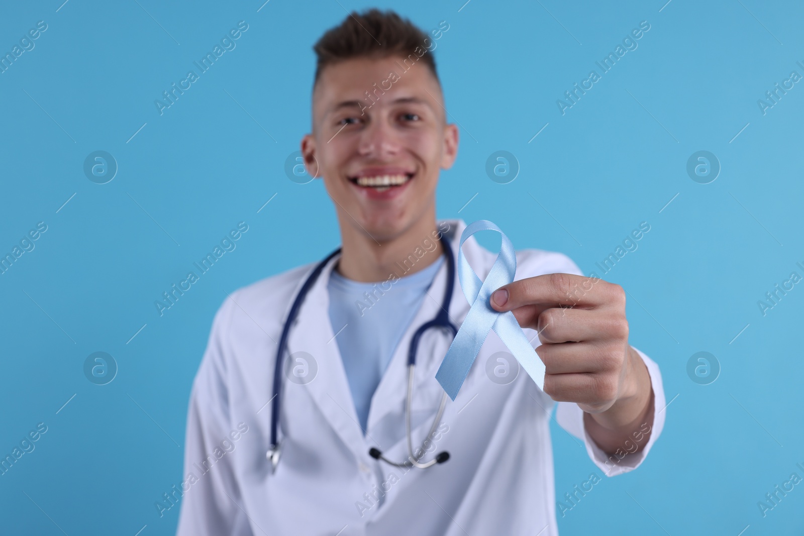 Photo of Prostate cancer awareness. Doctor holding light blue ribbon as symbol of support on color background, selective focus