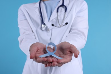 Photo of Prostate cancer awareness. Doctor holding light blue ribbon as symbol of support on color background, closeup