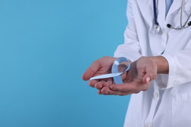 Photo of Prostate cancer awareness. Doctor holding light blue ribbon as symbol of support on color background, closeup. Space for text