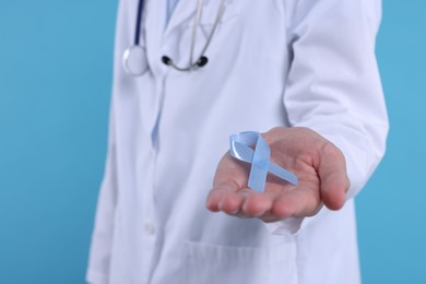 Prostate cancer awareness. Doctor holding light blue ribbon as symbol of support on color background, closeup