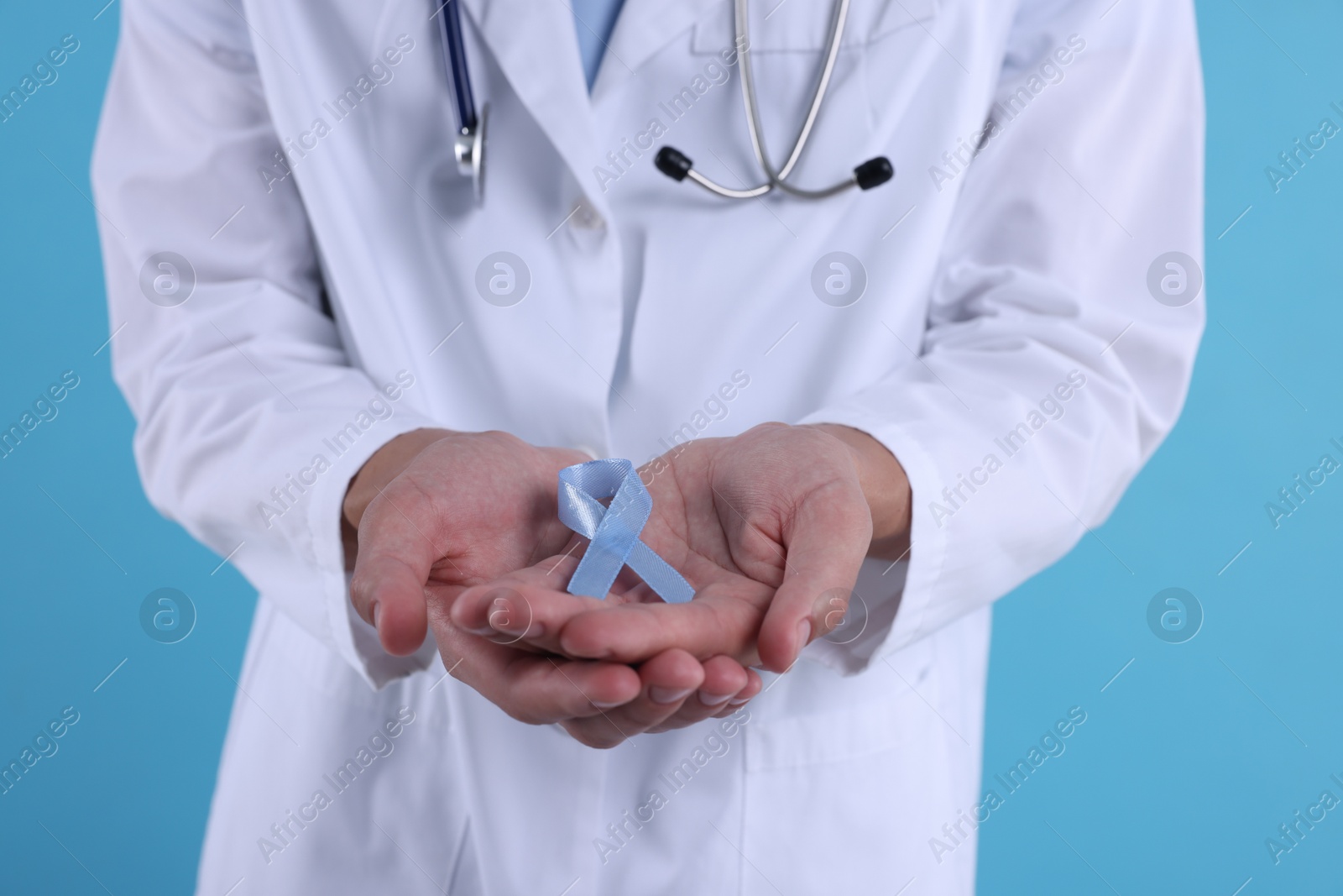 Photo of Prostate cancer awareness. Doctor holding light blue ribbon as symbol of support on color background, closeup