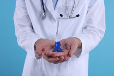 Photo of Prostate cancer awareness. Doctor holding blue ribbon as symbol of support on color background, closeup