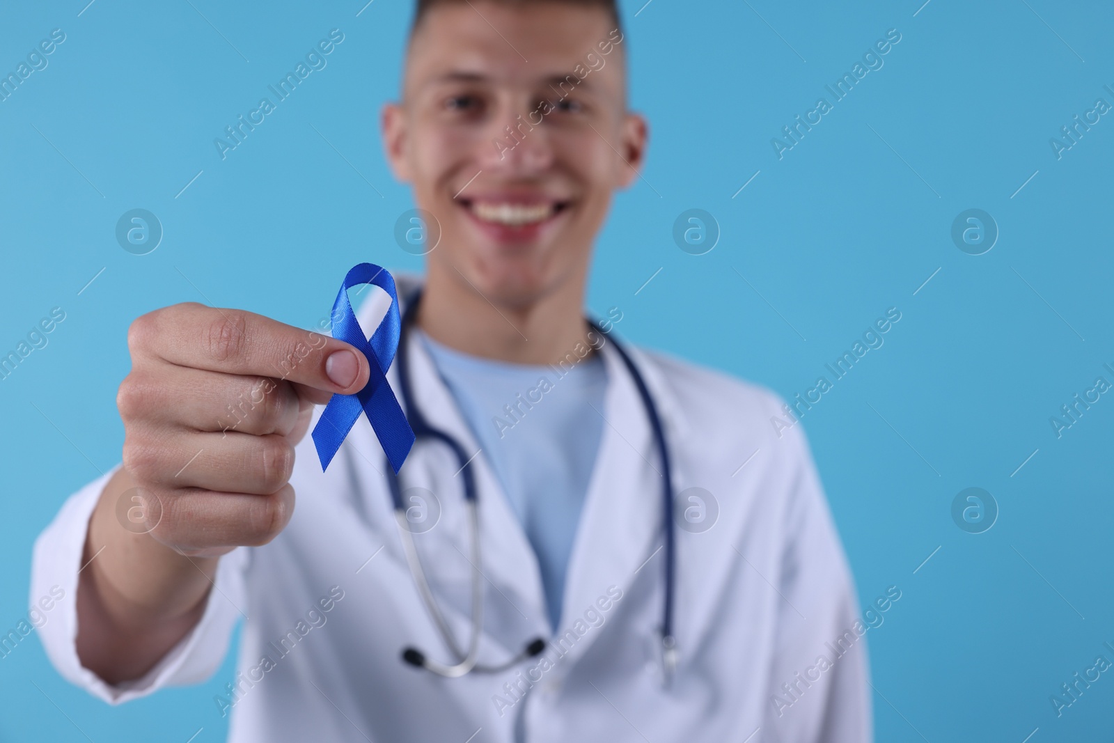 Photo of Prostate cancer awareness. Doctor holding blue ribbon as symbol of support on color background, selective focus