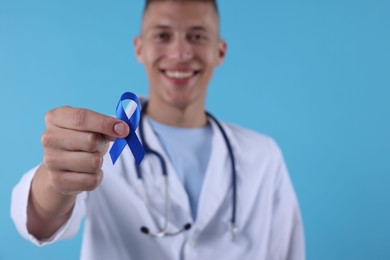 Photo of Prostate cancer awareness. Doctor holding blue ribbon as symbol of support on color background, selective focus