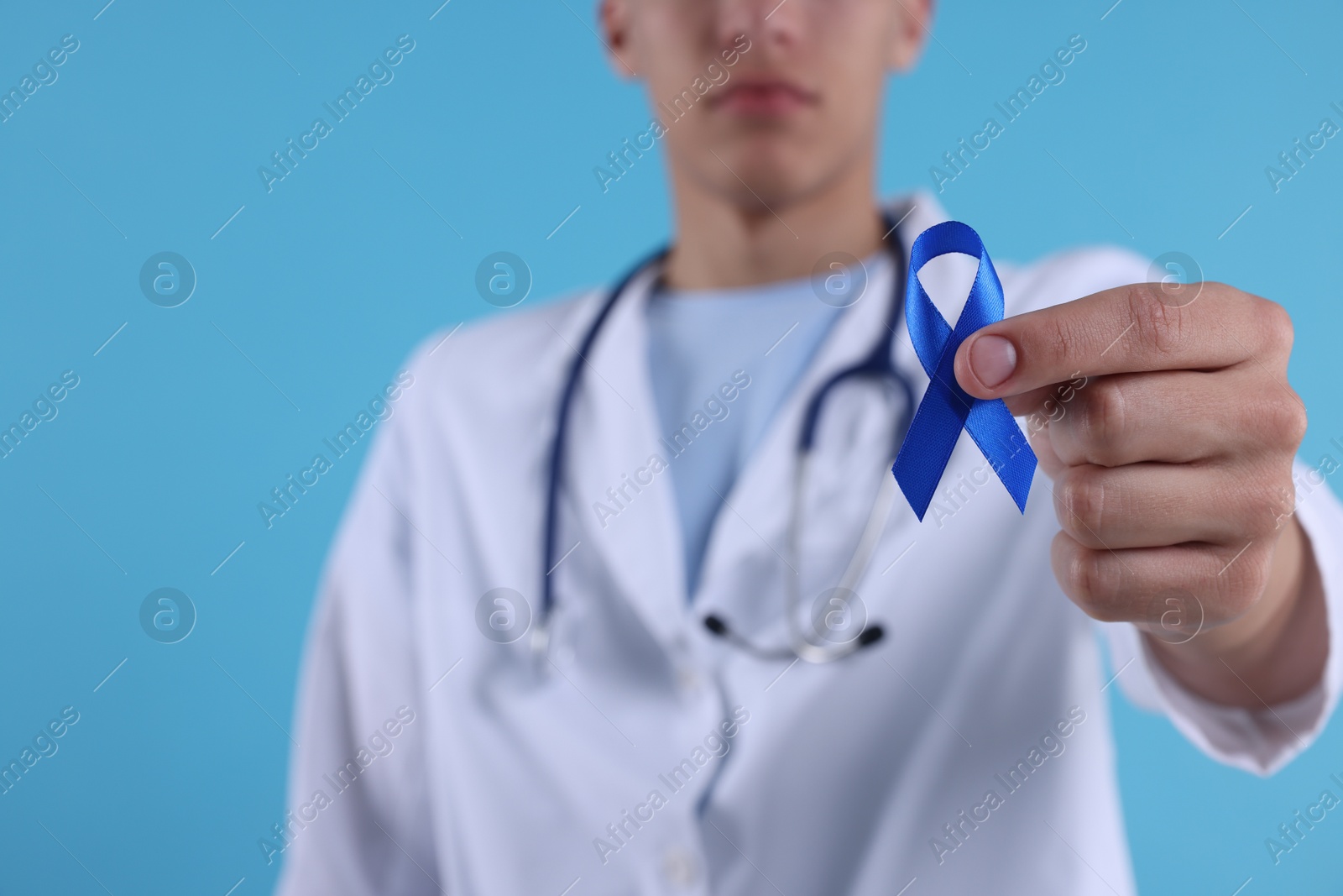 Photo of Prostate cancer awareness. Doctor holding blue ribbon as symbol of support on color background, selective focus