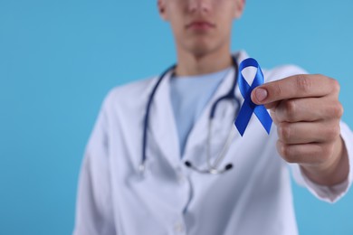 Photo of Prostate cancer awareness. Doctor holding blue ribbon as symbol of support on color background, selective focus