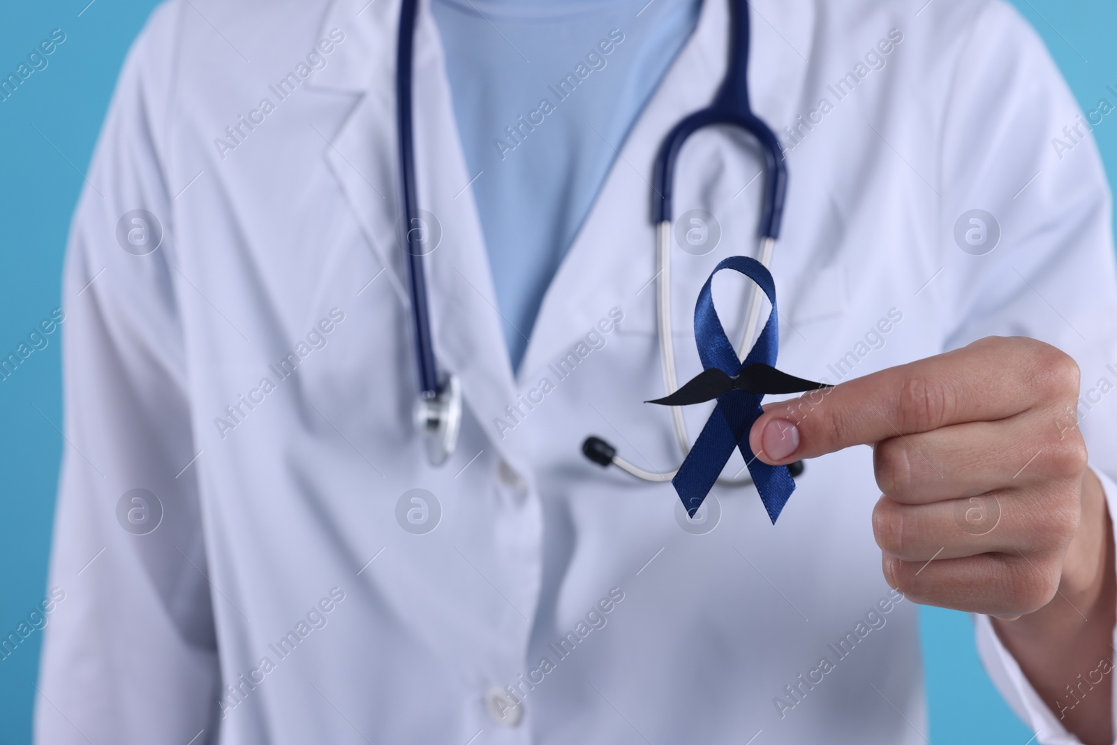 Photo of Prostate cancer awareness. Doctor holding blue ribbon with fake mustache on color background, closeup