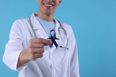 Prostate cancer awareness. Doctor holding blue ribbon with fake mustache on color background, selective focus. Space for text