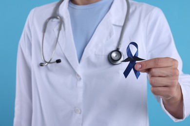 Photo of Prostate cancer awareness. Doctor holding blue ribbon with fake mustache on color background, closeup