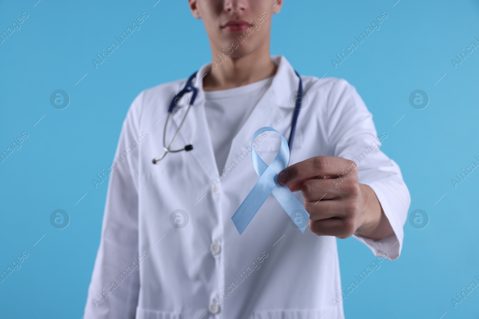 Photo of Prostate cancer awareness. Doctor holding light blue ribbon as symbol of support on color background, selective focus