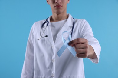Photo of Prostate cancer awareness. Doctor holding light blue ribbon as symbol of support on color background, selective focus