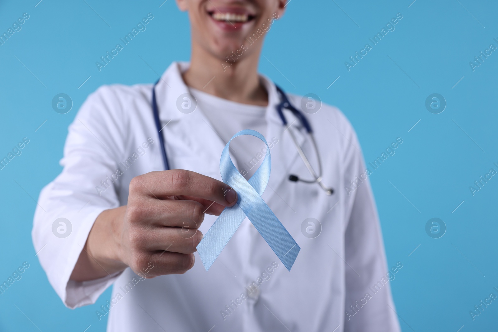 Photo of Prostate cancer awareness. Doctor holding light blue ribbon as symbol of support on color background, selective focus