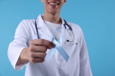 Photo of Prostate cancer awareness. Doctor holding light blue ribbon as symbol of support on color background, selective focus