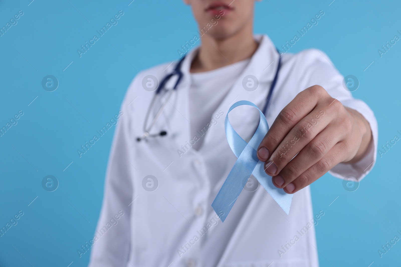 Photo of Prostate cancer awareness. Doctor holding light blue ribbon as symbol of support on color background, selective focus