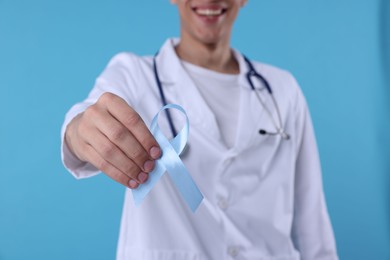 Photo of Prostate cancer awareness. Doctor holding light blue ribbon as symbol of support on color background, selective focus