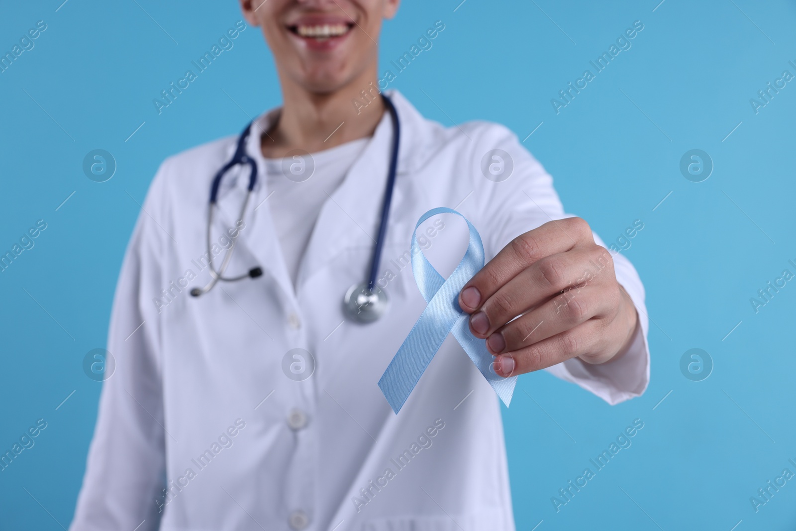 Photo of Prostate cancer awareness. Doctor holding light blue ribbon as symbol of support on color background, selective focus