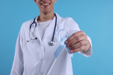 Photo of Prostate cancer awareness. Doctor holding light blue ribbon as symbol of support on color background, selective focus