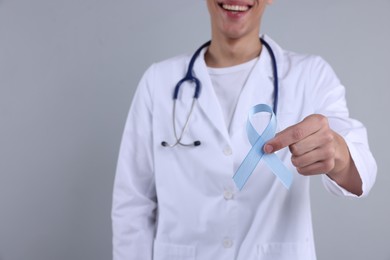 Photo of Prostate cancer awareness. Doctor holding light blue ribbon as symbol of support on grey background, selective focus