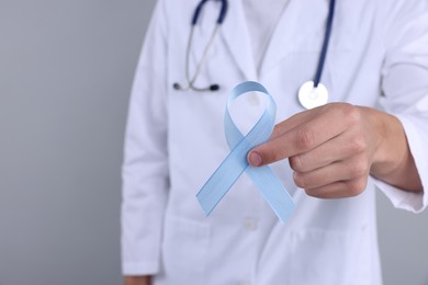 Photo of Prostate cancer awareness. Doctor holding light blue ribbon as symbol of support on grey background, closeup