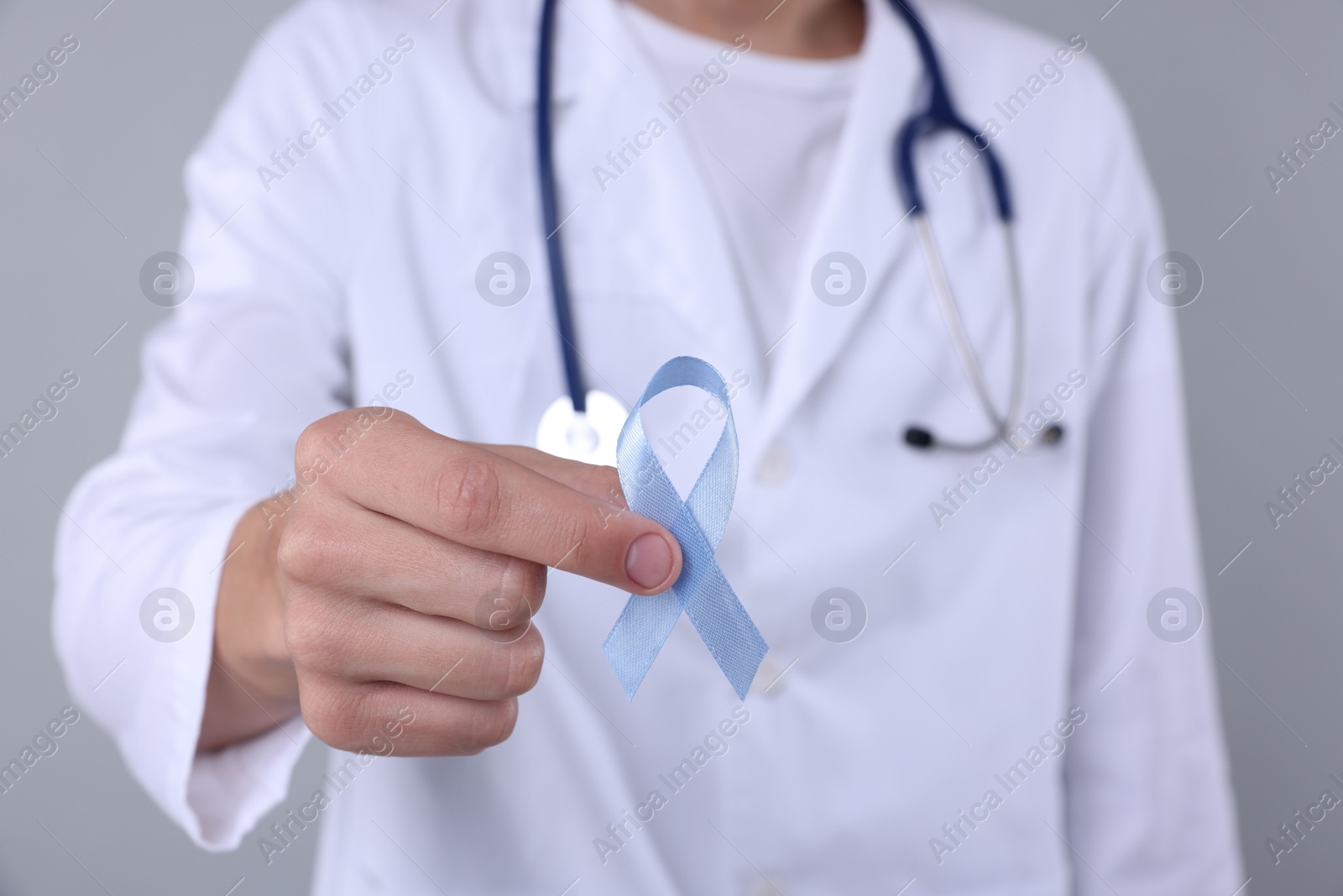 Photo of Prostate cancer awareness. Doctor holding light blue ribbon as symbol of support on grey background, closeup