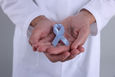 Photo of Prostate cancer awareness. Doctor holding light blue ribbon as symbol of support on grey background, closeup