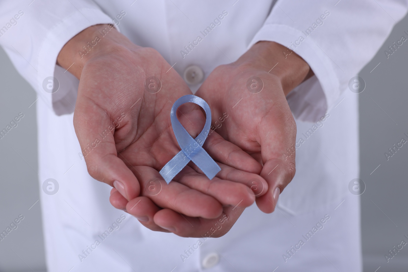 Photo of Prostate cancer awareness. Doctor holding light blue ribbon as symbol of support on grey background, closeup